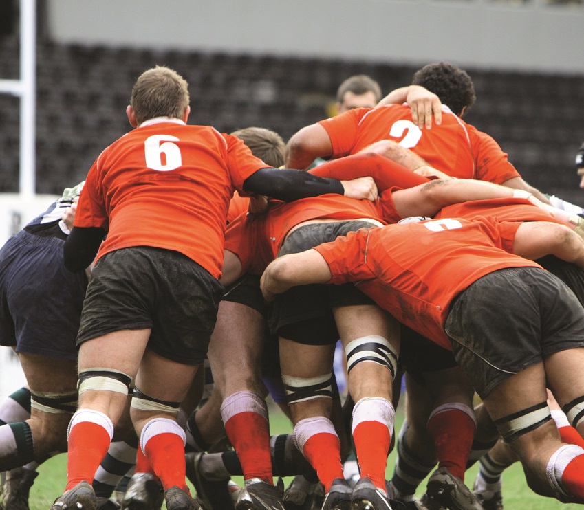Group of rugby players wearing orange shirts grouped together in a scrum.