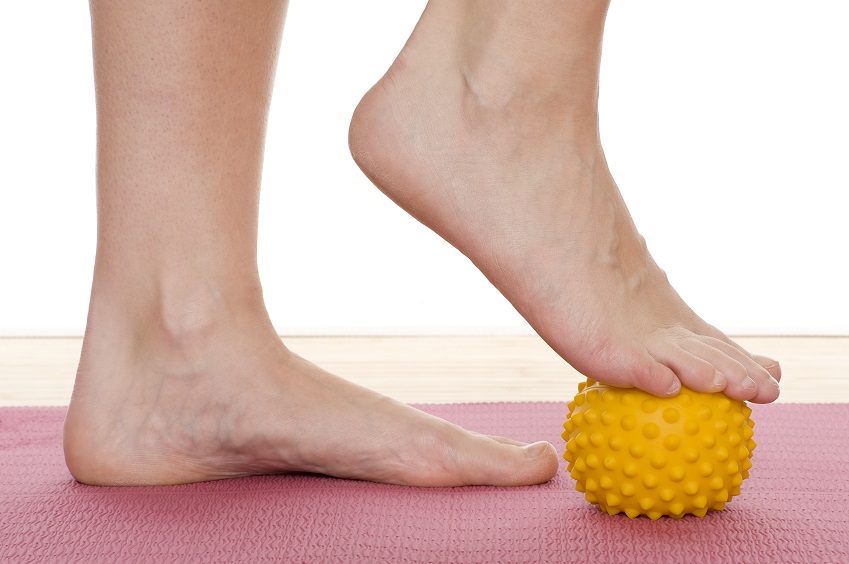 Feet with one foot placed on top of a yellow ball.